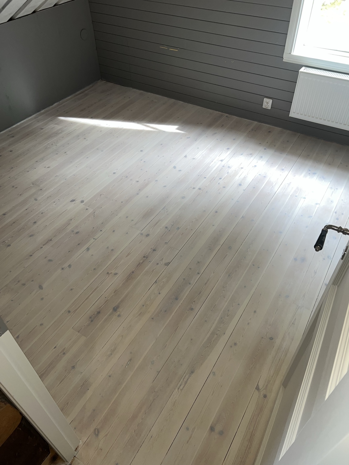 Ljust behandlade golvbrädor intill grå väggpanel
